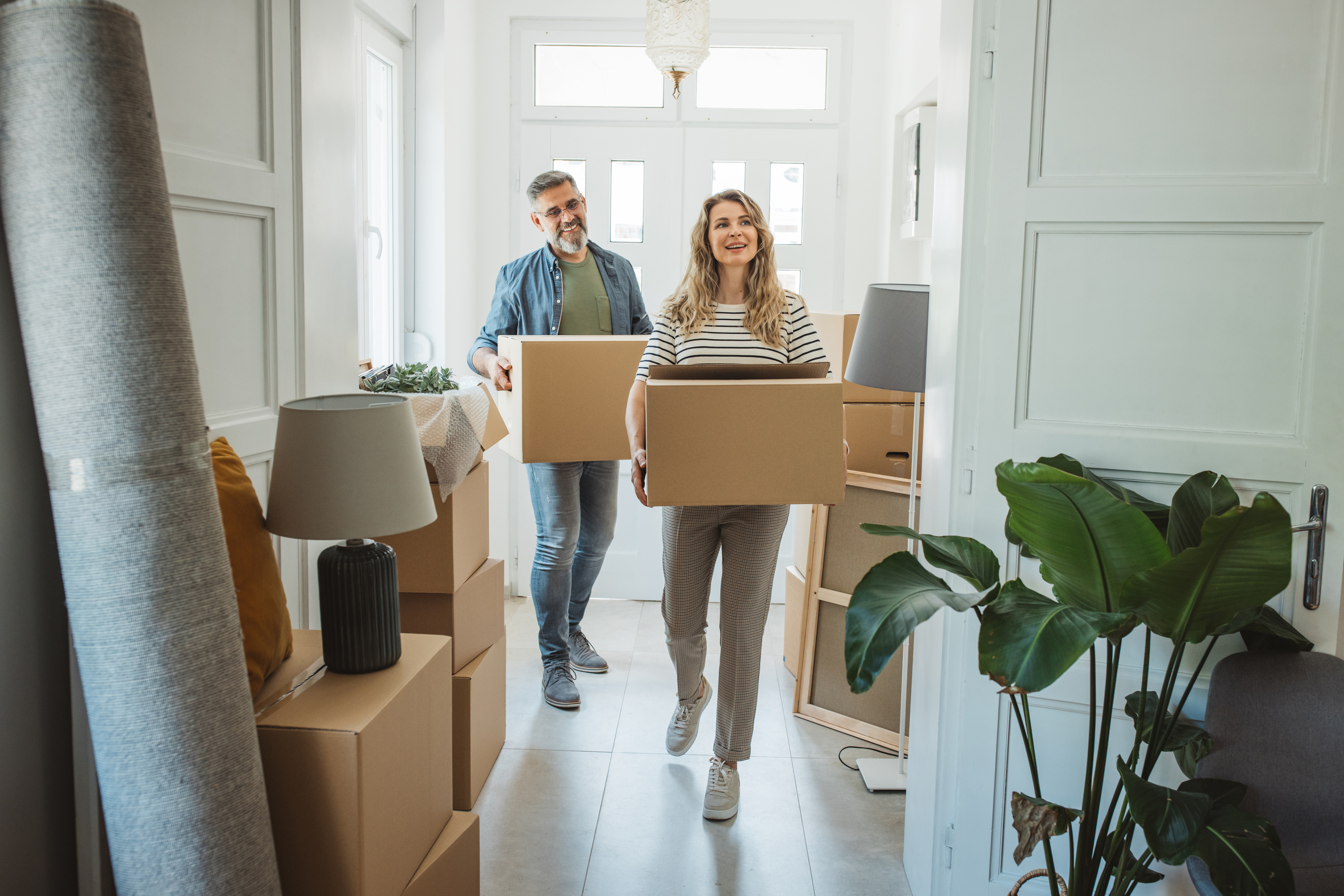 Couple carrying moving boxes into a bright clean home